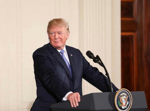 Person speaking at podium, presidential seal on front.