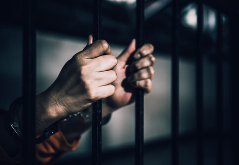 Hands gripping prison bars, suggesting confinement