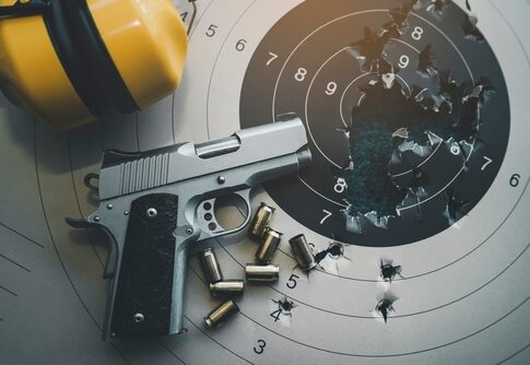 A handgun placed on a shooting target with bullet holes and spent cartridges nearby