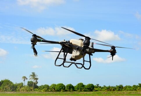 A drone flying over a green landscape under a blue sky